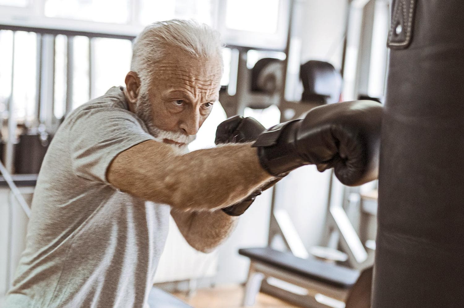 Oudere man bokst met bokshandschoenen tegen een bokszak tijdens Parkinson Fit Boxing.